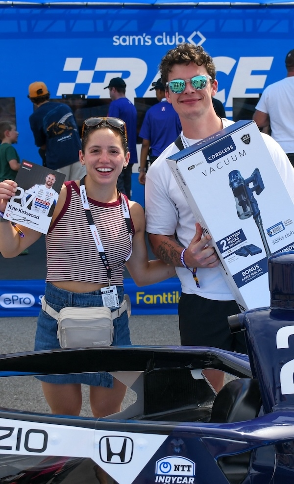 Two happy young people smile while holding products in front of a Sam's Club special event.
