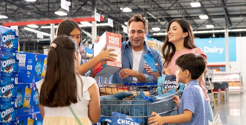 A family shopping together in a Sam's Club store, browsing aisles filled with various products and bulk items.