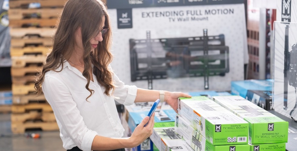 A Sam's Club member uses her phone to more closely inspect a TV wall mount in-club.