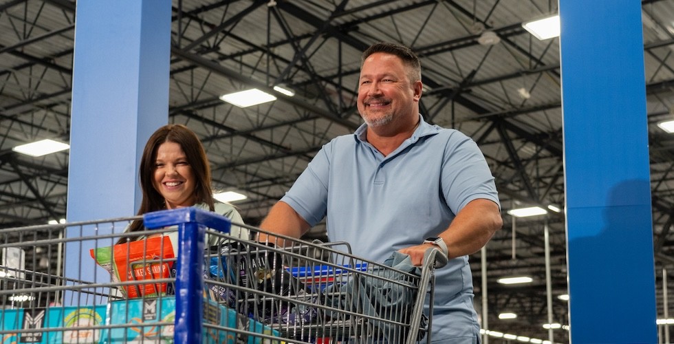 Two happy Sam's Club members enter the club with a cart, ready to begin their shopping experience.