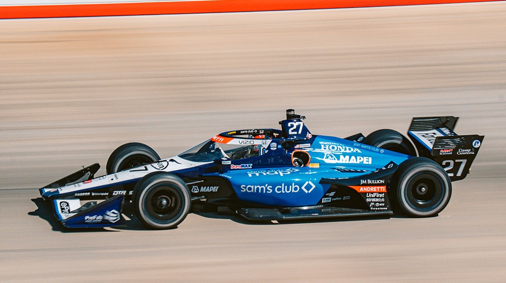 A mother and daughter smile as they push a cart and shop together inside of a Sam's Club.