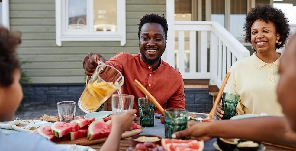 A family gathered around a picnic table, enjoying a meal together in a sunny outdoor setting.